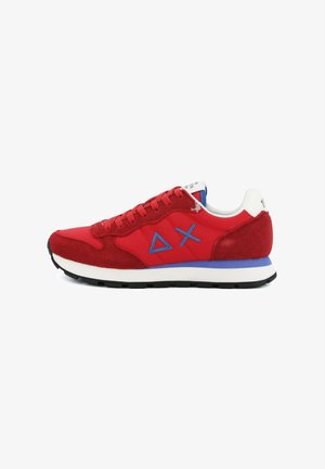 Zapatilla deportiva roja y azul con paneles de ante y tela, logo geométrico azul en el lateral, suela blanca acolchada y parte inferior con dibujo negro.