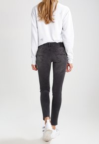 Černé úzké džíny se světlejším povrchem, s prošívanými oblastmi a jemnou texturou. V kombinaci s bílou mikinou a bílými teniskami.