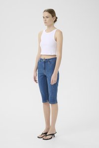 Bela rebrasta kratka majica, modri jeans kratke hlače do kolen z stranskimi žepi, sprednjim gumbom in elegantnimi črnimi japonkami.