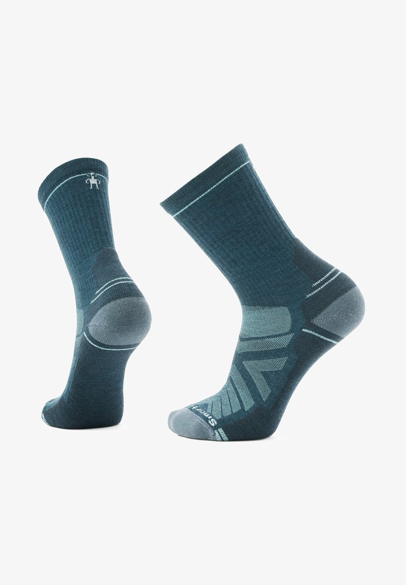 Mørk teal sokker med ribbet tekstur, forstærket hæl og tå, samt geometrisk mønster på siden med lyseblå accenter.