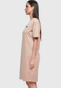 Svetloružové tričko-dress s krátkymi rukávmi, mierne voľný strih, vyrobené z bavlny, s logom na hrudi, jemná textúra, dĺžka po kolená.