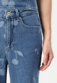 Blå denimjeans med et subtilt kirsebærblomsttrykk, med en klassisk fem-lomme design og metallknappfeste.