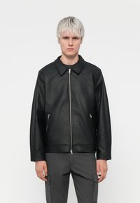 Black leather jacket with a pointed collar, front zipper, and two side pockets. The material appears textured, with a fitted silhouette.