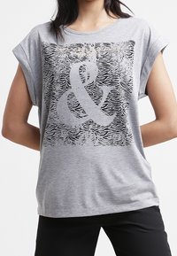 Harmaa graafinen t-paita lyhyillä hihoilla, jossa on suurikokoinen mustavalkoinen seepra-kuvio ja metallinhohtoinen "&" graafinen elementti. Pehmeä tekstuuri.