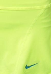 Top atlético amarillo neón hecho de tela elástica. Presenta una textura suave, un diseño aerodinámico y un pequeño logo azul de Nike.