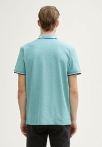 Turkos polo skjorta i stickad tyg med korta ärmar. Den har en krage med blå accenter och en rak fåll.