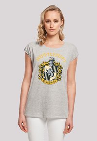 Grå bomulls T-skjorte med korte ermer som har et Hufflepuff-våpen i gult og svart, som viser et bor og dekorative elementer.