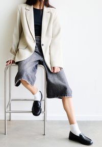 Beżowa, oversize'owa marynarka na czarną bluzkę, w zestawieniu z szarymi szortami o szerokich nogawkach i czarnymi loafersami. Białe skarpetki do kostek z falbanką.