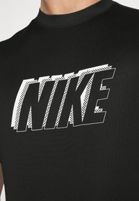 Camiseta negra de manga corta con un gran logo blanco de "NIKE" en un patrón de tablero de ajedrez sobre una tela texturizada.