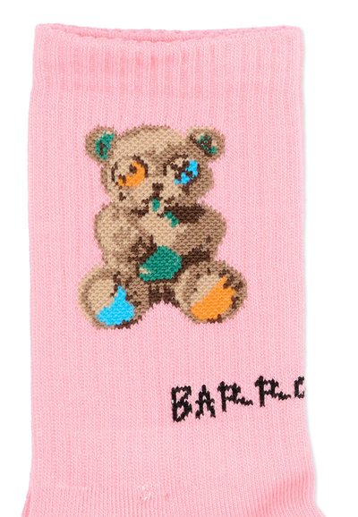 Roze sok met een gebreid ontwerp van een teddybeer met oranje, blauwe en groene vlekken en deels zichtbare zwarte tekst nabij de teen.