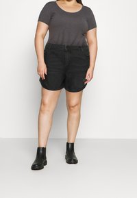 Czarne szorty jeansowe o luźnym kroju, z pięcioma kieszeniami i subtelnymi postrzępionymi krawędziami. Zestawione z szarym topem z krótkim rękawem i czarnymi botkami za kostkę.