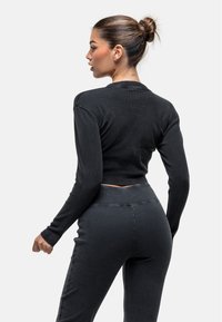 Top corto a maniche lunghe ribassato nero abbinato a leggings a vita alta coordinati; entrambi mostrano una morbida trama e un design aderente.