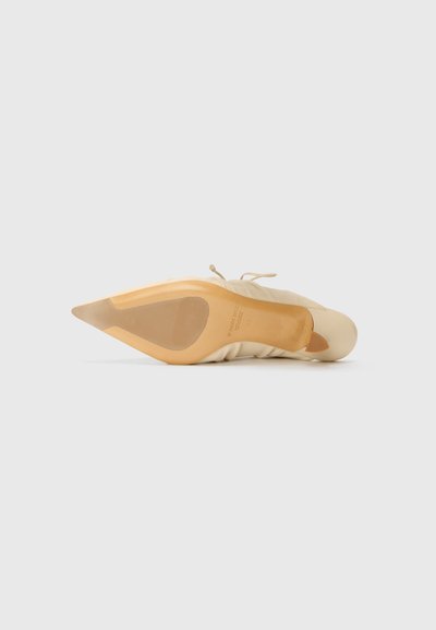 Zapato de tacón alto beige con punta afilada, hecho de tela suave, que presenta una silueta elegante y una suela de color claro con un detalle de marca mínimo.