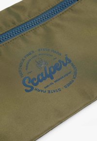Saco de tela verde oliva con una cremallera azul. Presenta un logo circular con texto y un gráfico de calavera, que muestra "Scalpers" y detalles de ubicación.
