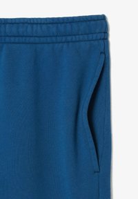 Pantalones de chándal azules hechos de una tela suave, con una cinturilla elástica, bolsillos laterales y una textura lisa con detalles de costura.