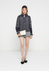 Navy floral blouse with button closure, ruffle accents, long sleeves; paired with a gray skirt and black bow-detail heels. White clutch.