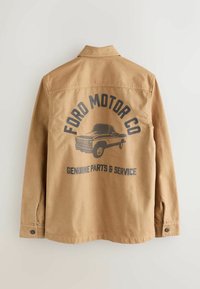 Hnědá bunda s límečkem a dlouhými rukávy. Obsahuje černou grafiku náklaďáku a text "FORD MOTOR CO" a "ORIGINÁLNÍ DÍLY A SLUŽBY."