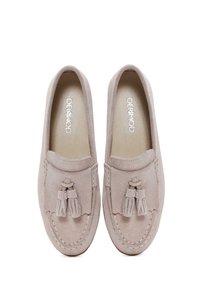 Mocasines de ante beige con acentos de borlas, punta redonda y costuras en contraste a lo largo de la suela. Forro interior suave y suela plana.