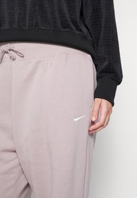 Nike joggingbukser i lyserød med elastisk talje, snører og sidelommer. Har et sølvfarvet Nike-logo på venstre lår.