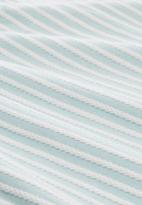 Ljust blått tyg med vita horisontella ränder; den texturerade mönstret skapar ett ribbat utseende med vågiga kanter på ränderna.