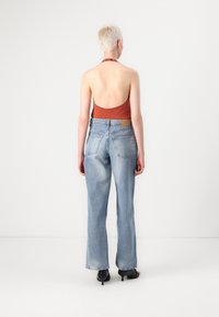Vue de dos d'une personne portant un haut halter de couleur rouille et un jean évasé bleu clair. Le jean possède deux poches arrière et une étiquette à la taille.