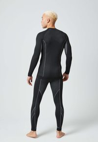 Zwarte aansluitende thermoshirt en legging, met witte accentstiksels en een gestructureerd ontwerp, geschikt voor actieve kleding.