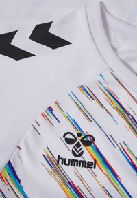 Hvid atletisk skjorte med rund hals, sorte chevron-accenter og et flerfarvet grafik nederst. Har et sort logo.