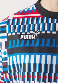 Camiseta gráfica de Puma con un diseño vibrante que presenta patrones en negro, azul, rojo y blanco; incluye un logo bordado en negro en la parte frontal.