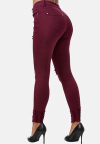 Jeans slim burdeos con acabados deshilachados, textura suave, cinco bolsillos y herrajes plateados, combinados con tacones altos negros.