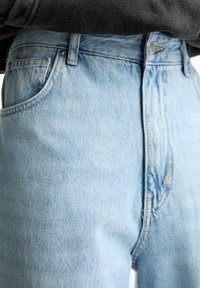 Jeans de tiro alto en azul claro con un diseño clásico de cinco bolsillos, costuras visibles y una textura de denim desgastado.