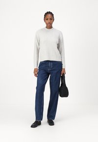 Lys grå strikkegenser med ribbestruktur, kombinert med løse mørkeblå jeans. Modellen holder en svart flettet håndveske og har på seg svarte sko.