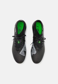 Black athletic shoes with textured synthetic upper, featuring a green insole, black laces, and white angular accent patterns.