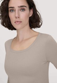 Lichtbeige langemouwen top met een ronde hals en een zachte textuur, voorzien van aansluitende mouwen en een eenvoudig ontwerp.