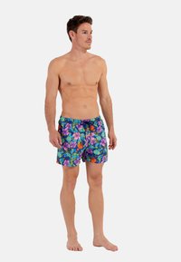 Costumi da bagno da uomo in blu vivace con motivi floreali che presentano fiori viola, rosa e arancioni. Leggeri, con vita regolabile e lunghezza fino a metà coscia.