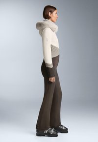 Világos bézs színű kapucnis dzseki műszőrme gallérral, sötétbarna, testhez simuló nadrággal párosítva. A dzsekire jellemző jellegzetes átlós varrásdíszítés. Fekete csizmák.