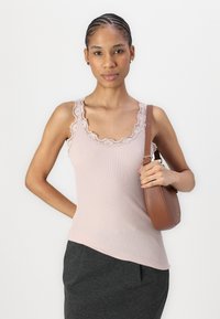 Helles rosa, quer geripptes Tanktop mit Spitzendetail. Das Model hält eine braune, runde Handtasche. Weicher Stoff, figurbetontes Design und leicht asymmetrischer Saum.