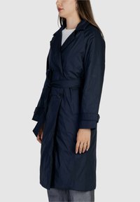 Cappotto trench blu navy con vita regolabile, bottoni doppi e ampi revers; presenta maniche lunghe e un tessuto morbido e leggero.