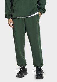 Zielone spodnie dresowe z luźnym krojem, elastycznym pasem w talii i bocznymi kieszeniami. Materiał wydaje się być miękki, z subtelnym detalem logo.