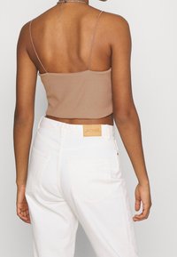 Crop top marron à côtes avec des fines bretelles, associé à un jean en denim blanc taille haute avec un patch en cuir sur la ceinture arrière.