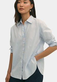 Lichtblauw en wit gestreept overhemd met een klassieke kraag, lange mouwen en een gebogen zoom; gemaakt van een zachte, gestructureerde stof.