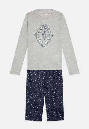 Bluză gri cu mânecă lungă și fundal cu buline navy. Partea de sus are un logo floral albastru. Textură netedă, design casual.