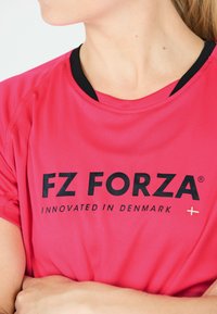 FZ Forza -brändi urheilupaita kirkkaan vaaleanpunaisena mustalla kaula-aukolla. Sisältää lyhyet hihat ja sileää, kevyttä kangasta.