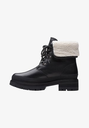 Black leather ankle boot with a fluffy cream-colored cuff, textured surface, rounded toe, and a rugged black rubber sole.