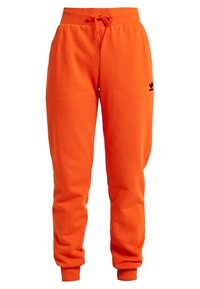 Oranžové bavlněné tepláky s elastickým pasem, nastavitelnou šňůrkou a černým logem na levé nohavici. Zúžený střih směrem k kotníkům.
