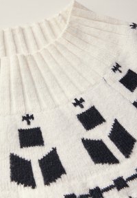 Ivory-neulepaita, jossa on ribbikuvioitu kaulus ja mustia geometrisia kuvioita. Pehmeä rakenne, jossa on kontrastisia suunnitteluelementtejä koko ajan.