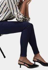 Jeans skinny azul oscuro con una textura suave, combinados con unos tacones de slingback negros de punta, con un tacón bajo y detalle de corte.