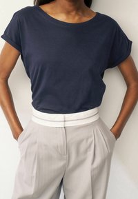 Donkerblauwe T-shirt met korte mouwen en een relaxte pasvorm, gecombineerd met lichtgrijze plooibroek met een witte tailleband.
