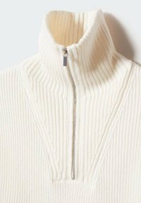 Crèmekleurige geribbelde trui met een hoge kraag en een zilveren rits. De gestructureerde stof heeft verticale strepen en een V-vormig ontwerp aan de voorkant.