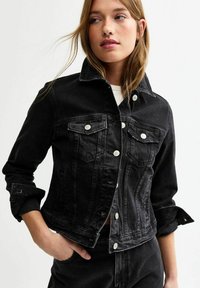 Chaqueta de mezclilla negra con un diseño ajustado, cierre frontal de botones, dos bolsillos en el pecho y puños de mangas enrollados para un look estructurado.