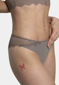 Sous-vêtements gris avec des bordures en dentelle, fabriqués dans un tissu lisse. Présentent une taille en dentelle festonnée et un tatouage de papillon sur la cuisse.